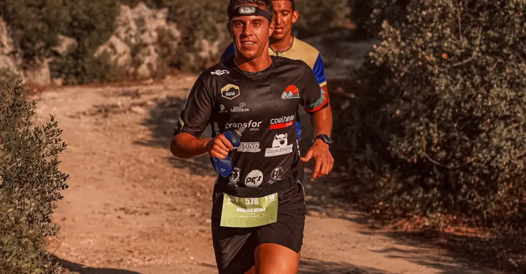A trail runner checking a GPS smartwatch on the wrist during a run in a dense green forest, sunlight filtering through trees, motion blur on background, realistic sports photography, editorial style