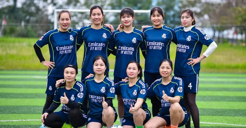 A group of female football players in different positions on a training pitch with GPS tracking devices, coach with tablet analyzing data, realistic sports photography, daytime