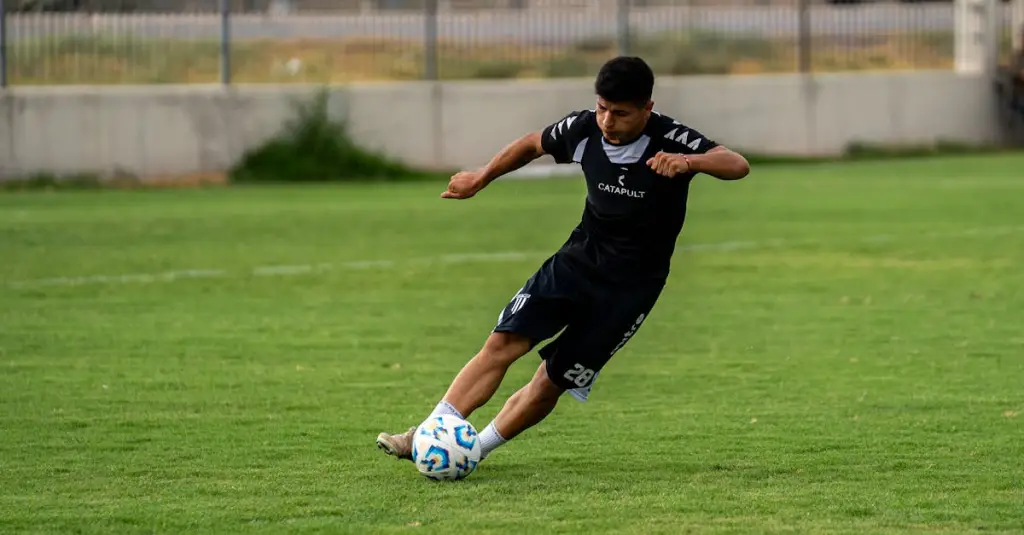 A football midfielder sprinting with the ball during a competitive match, motion blur on legs showing speed, crowd in the background, stadium atmosphere, photorealistic sports action photography