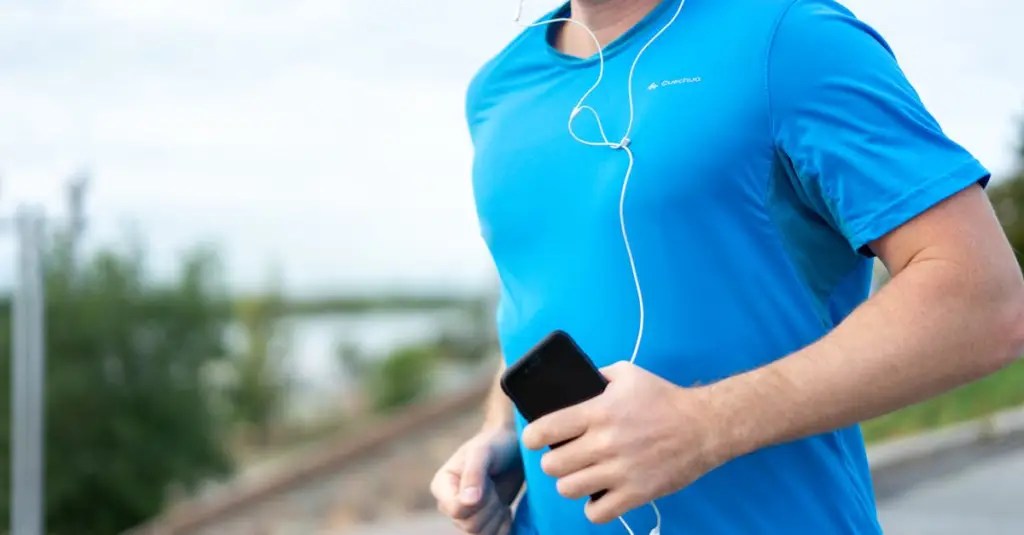 Close-up of a runner's hands holding a smartphone showing a heart rate training zone chart, running track blurred in background, fitness tracking concept, photorealistic stock photo