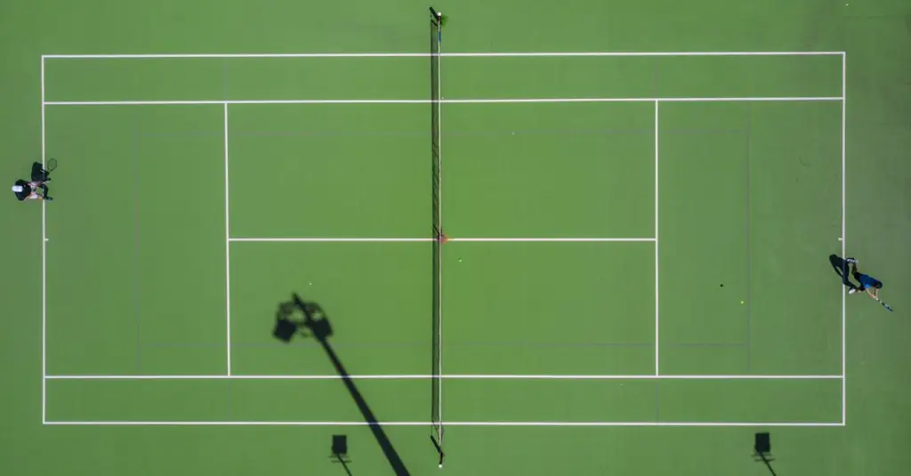 Overhead view of two tennis players on opposite sides of a clay court during a rally, red court surface, dramatic lighting, aerial sports photography, action shot with motion blur